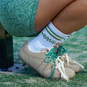 Person wearing green shorts and beige shoes on a tennis court